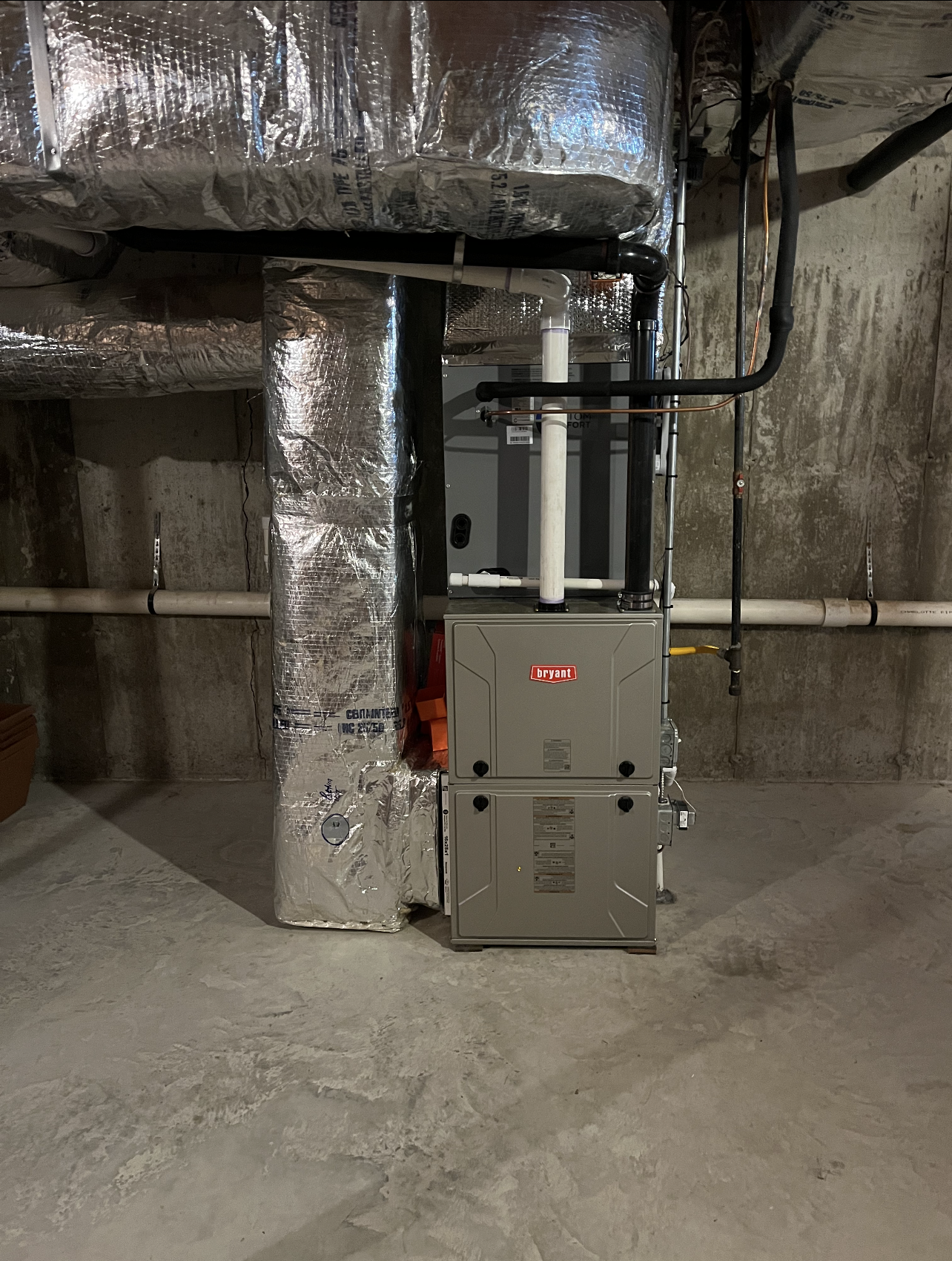 A furnace is sitting in a basement next to a pipe.