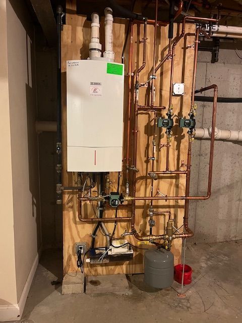 A white boiler is mounted on a wooden wall next to copper pipes.