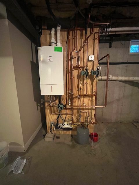 A white boiler is sitting on a wooden wall next to a bunch of pipes.
