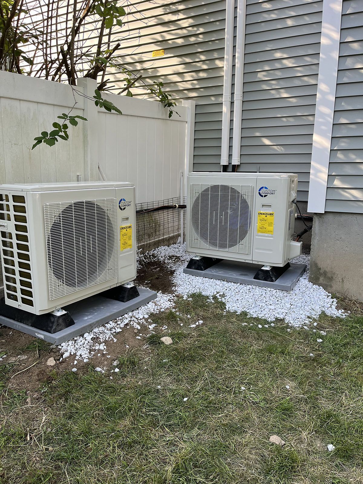 Two air conditioners are sitting outside of a house.