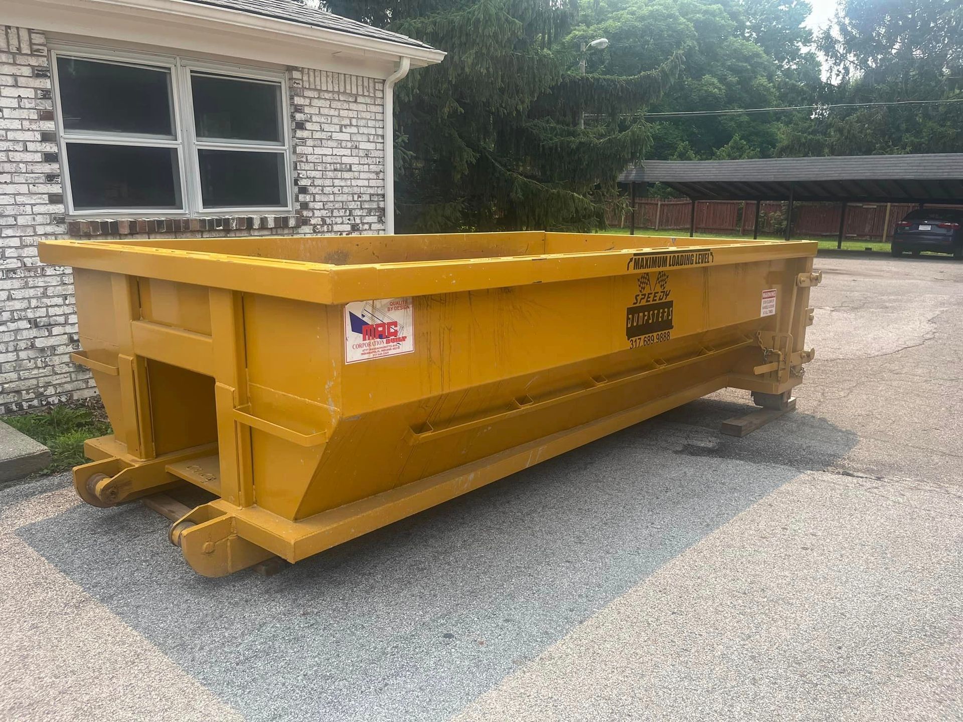 Yellow dumpster parked on gravel in front of a white brick building.