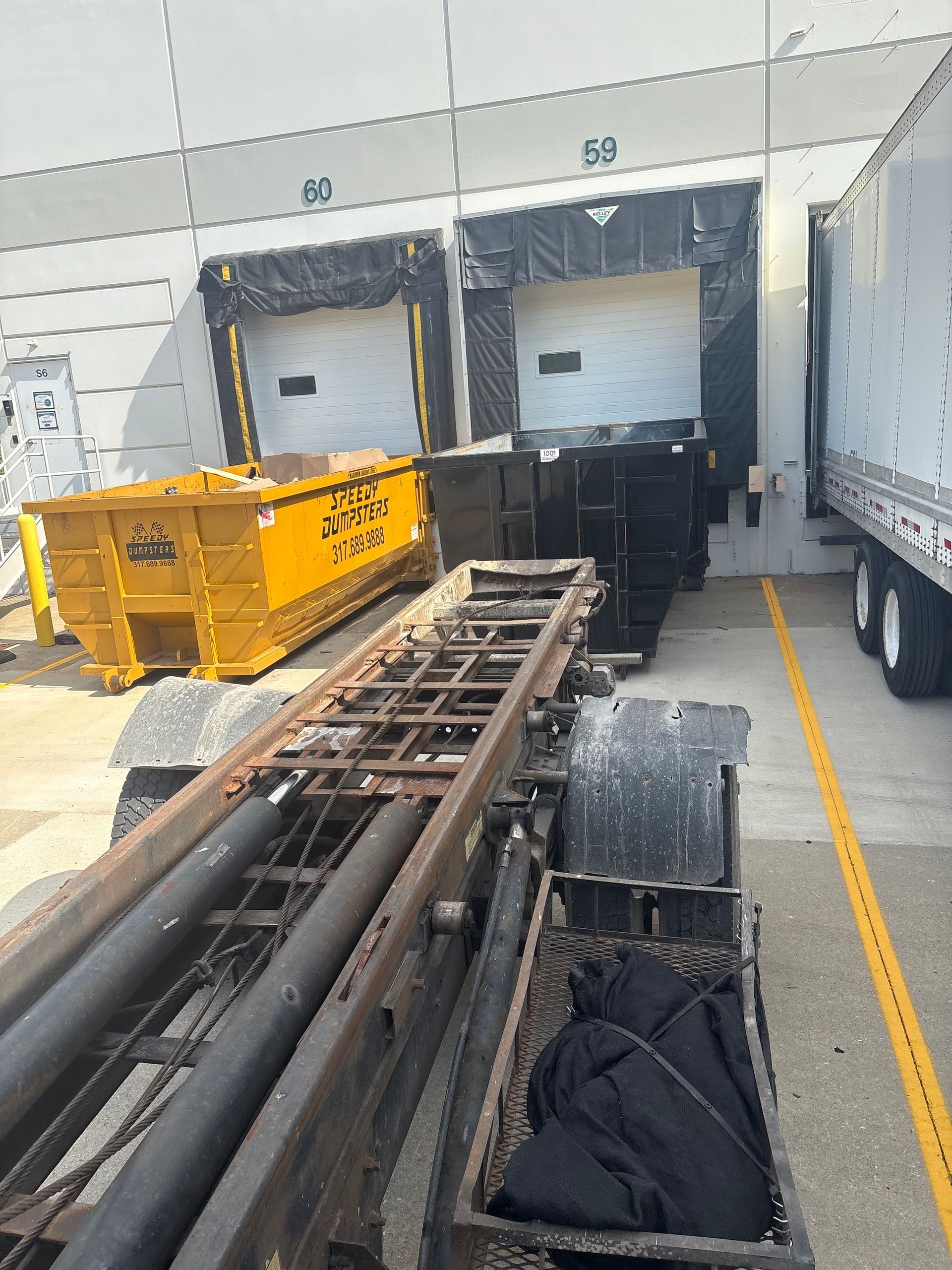 A truck loading dock with two open bays; a yellow dumpster and a roll-off truck in view.