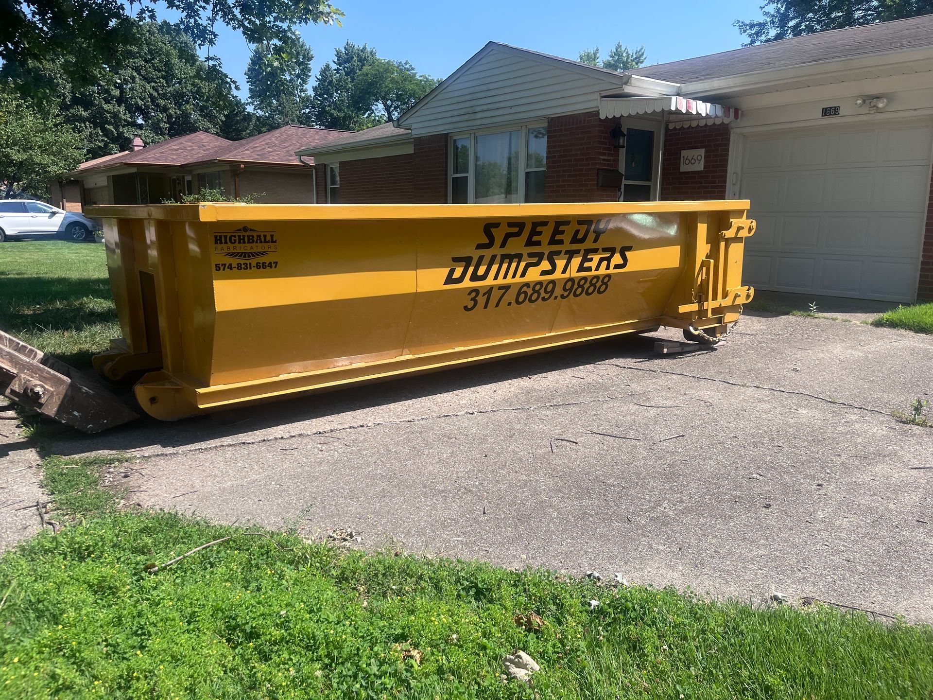 Yellow dumpster from Speedy Dumpsters on a driveway in front of a house.