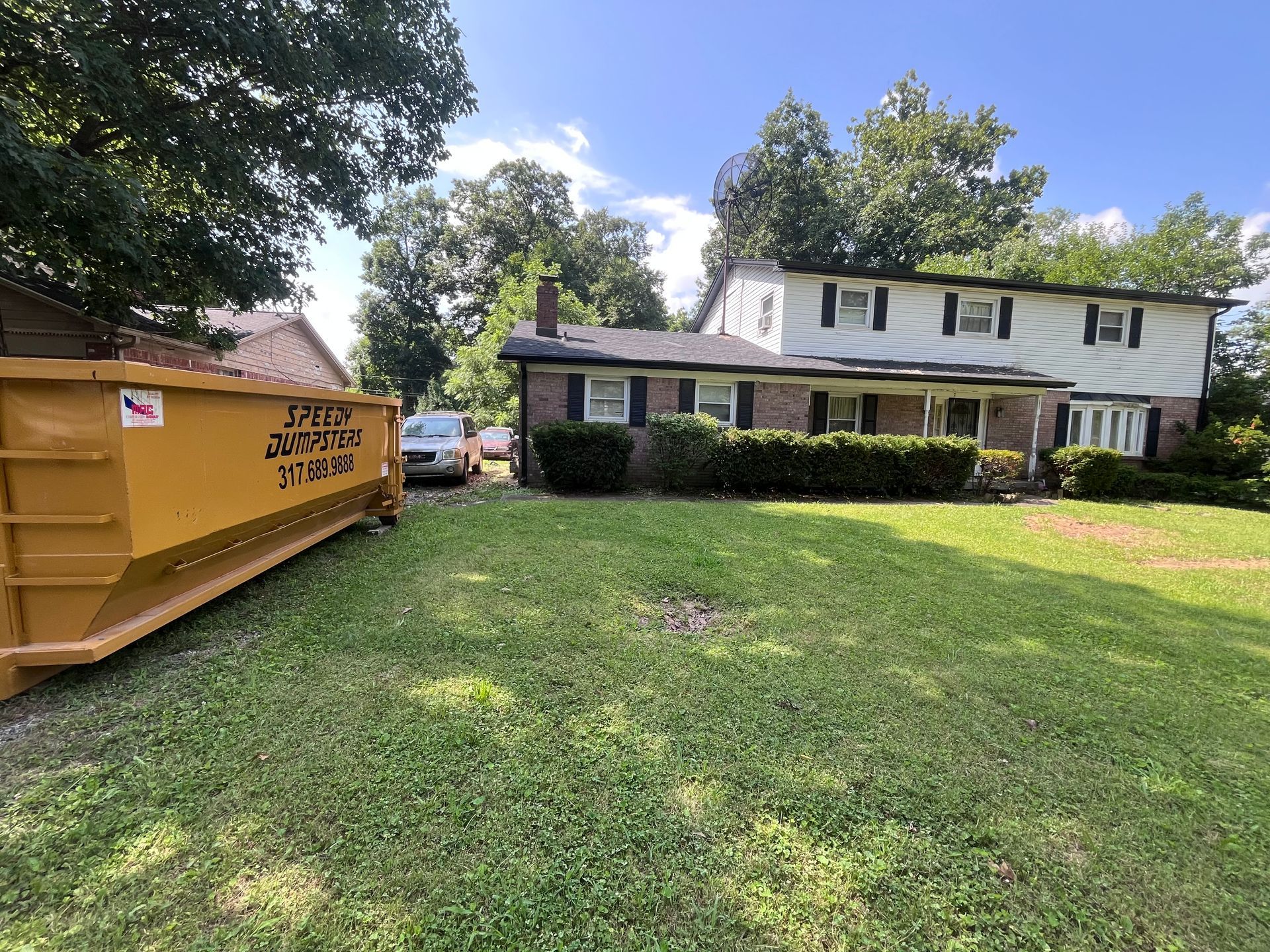 Yellow dumpster in front yard of two-story house with white siding and black shutters.