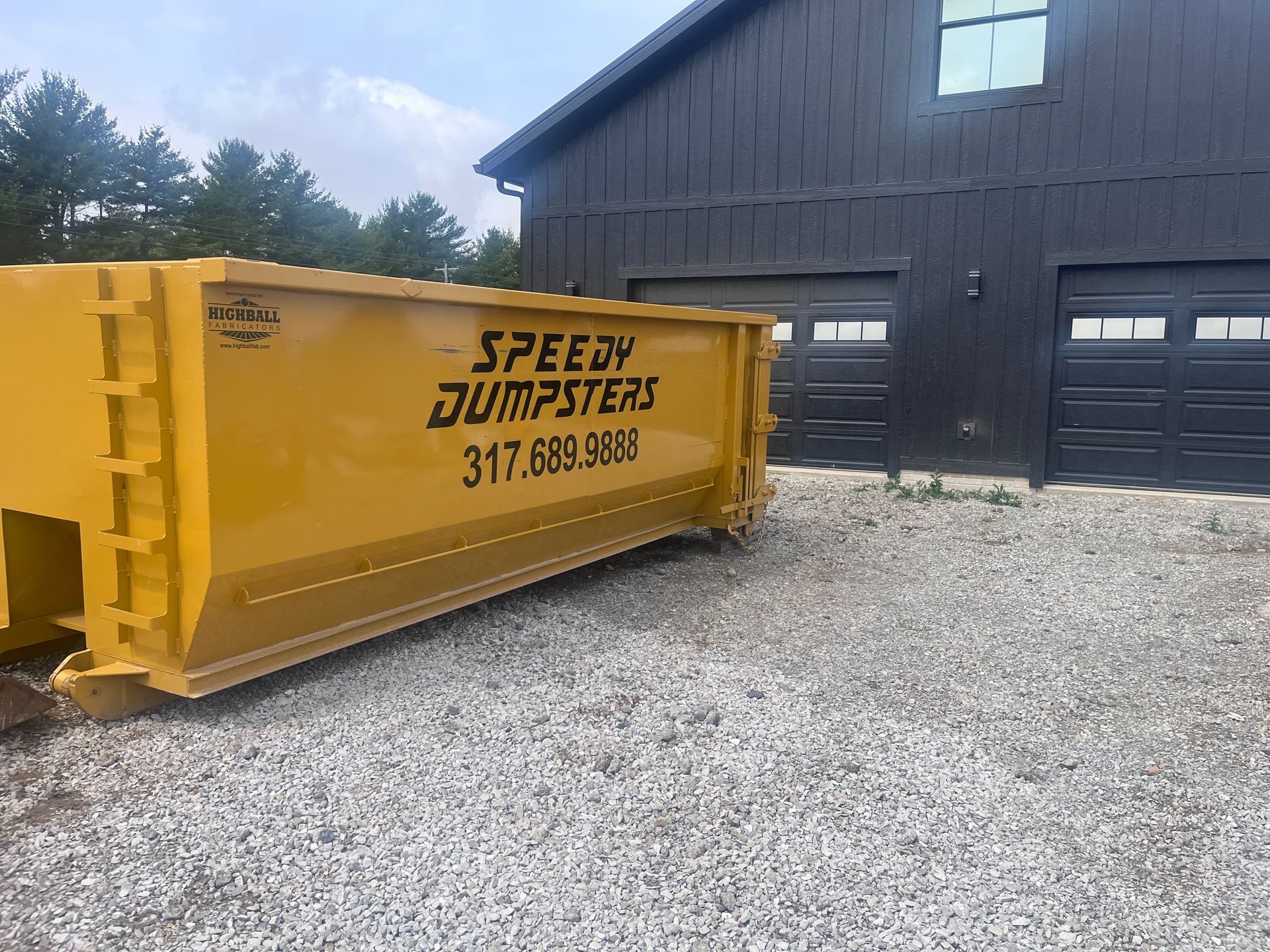 Yellow Speedy Dumpsters dumpster parked in front of a black building with gravel driveway, 317.689.9898.
