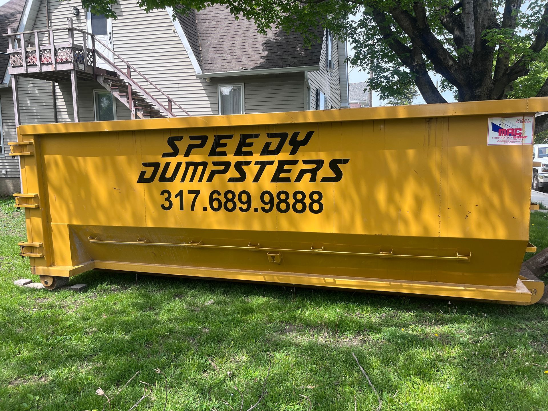 Yellow Speedy Dumpsters dumpster on grass, contact phone number visible.