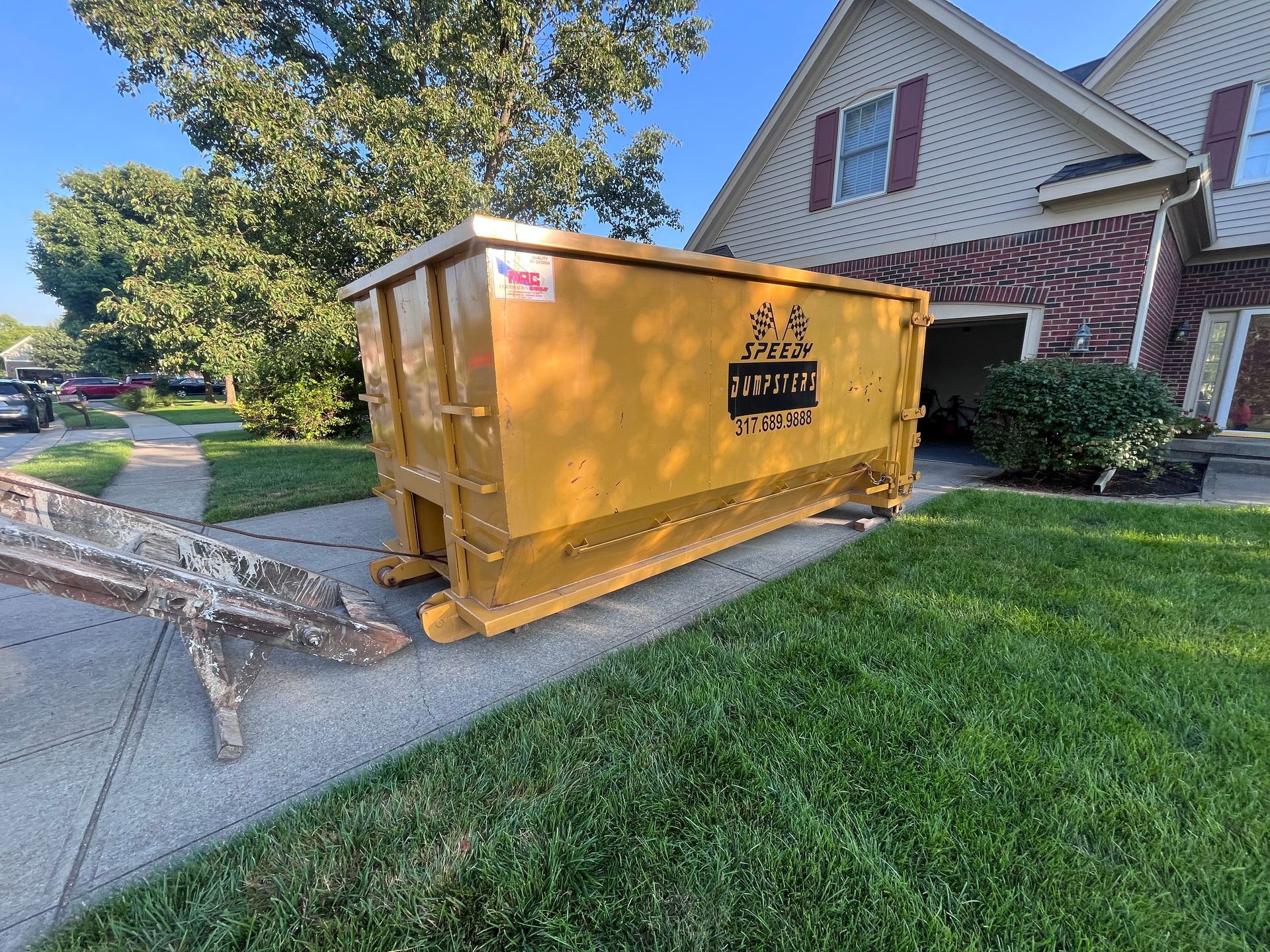 Yellow dumpster on residential property's grass next to sidewalk and house.