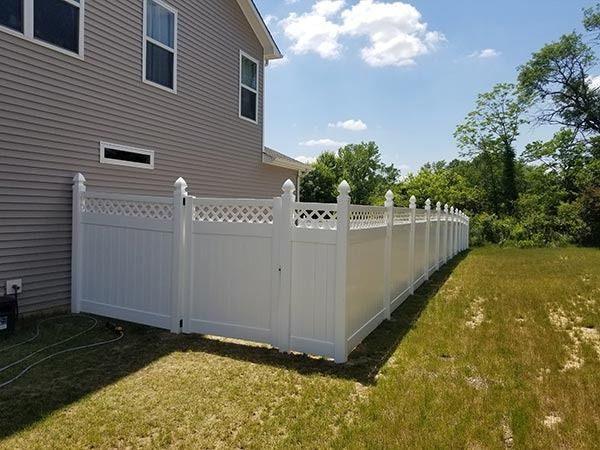 White vinyl fence around a grassy backyard, adjacent to a beige house, under a sunny sky.