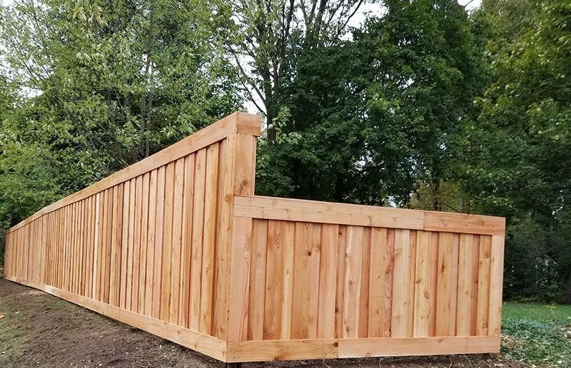Wooden privacy fence in front of a green leafy background.