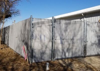 Chain link fence with privacy slats, two gates, next to a building.