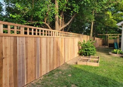 Wooden fence in a backyard with lattice top, near a tree, garden boxes, and a playset.