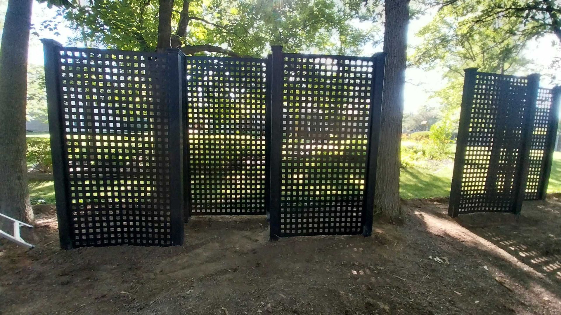 Black lattice screens between trees in a park setting.