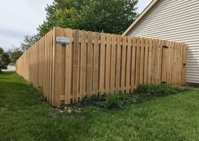 Wooden fence in a yard next to a building, with a door and green grass.