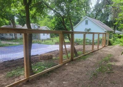 Wooden fence with wire mesh in a backyard, near a house and trees.
