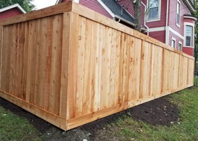 Wooden privacy fence surrounding a red house on a green lawn.
