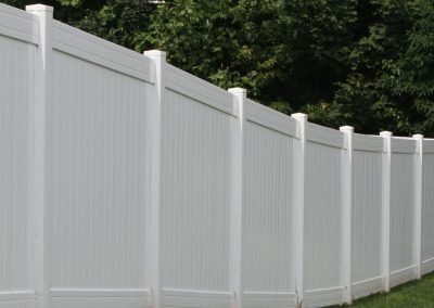 White vinyl privacy fence in a yard with green trees.
