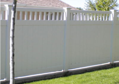 White vinyl fence in a grassy yard, with a picket top and solid lower panels.
