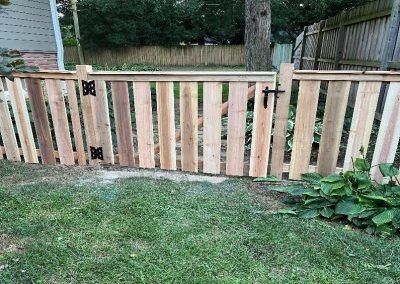 Wooden fence with gate in grassy yard. Vertical planks of varying wood tones, black hardware.