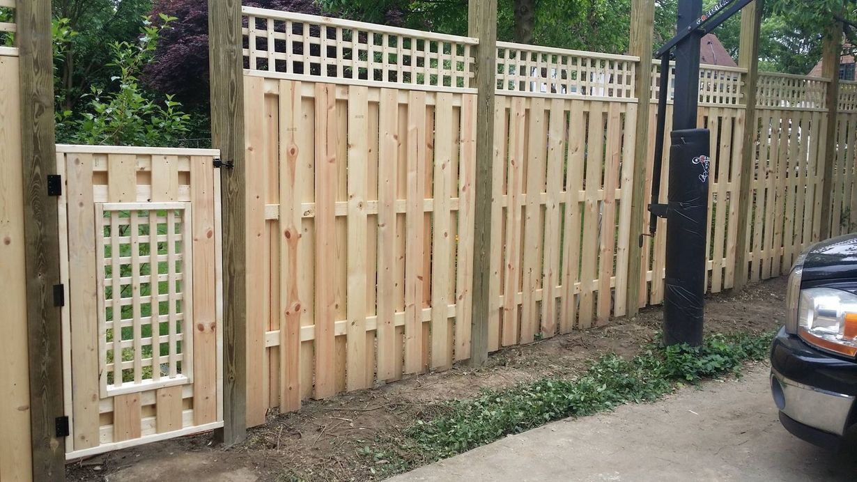 Wooden backyard fence with a small gate beside a driveway and parked car
