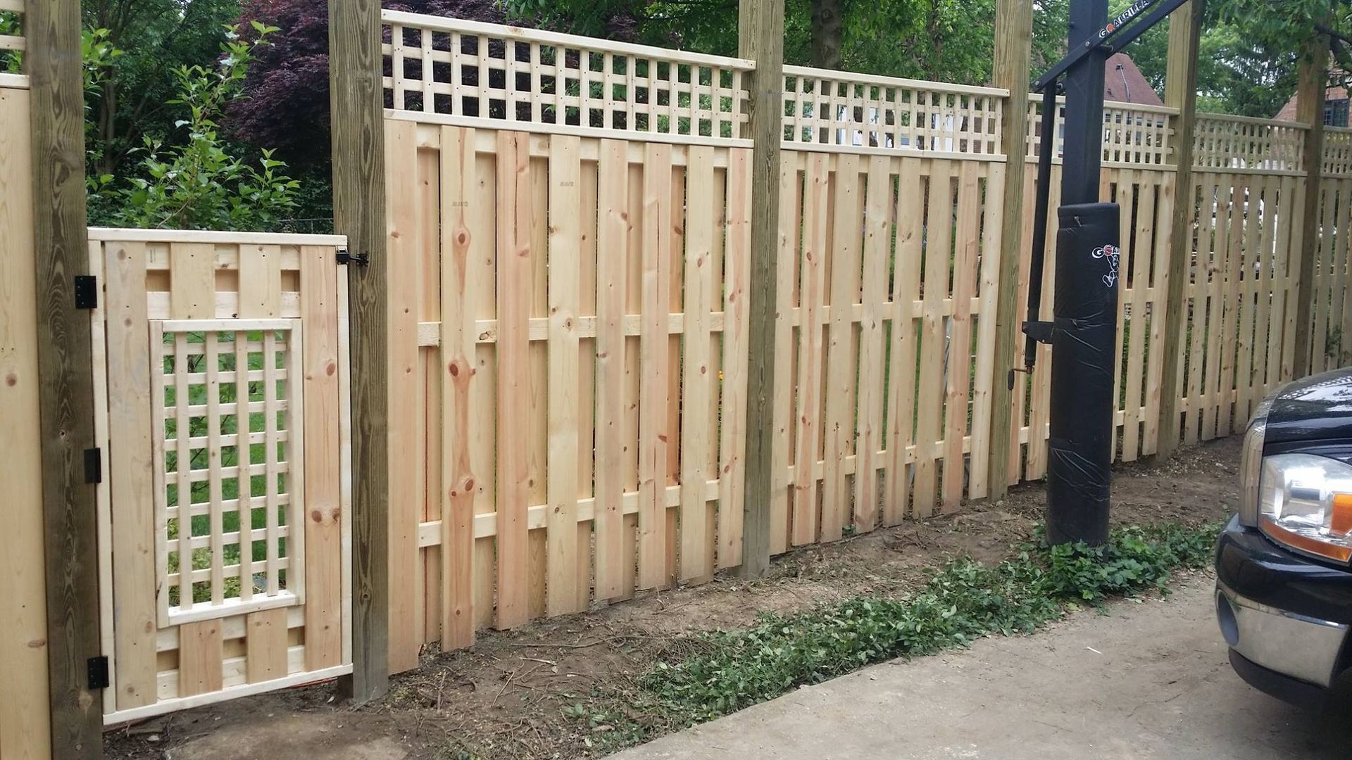 Wooden backyard fence with a small gate beside a driveway and parked car