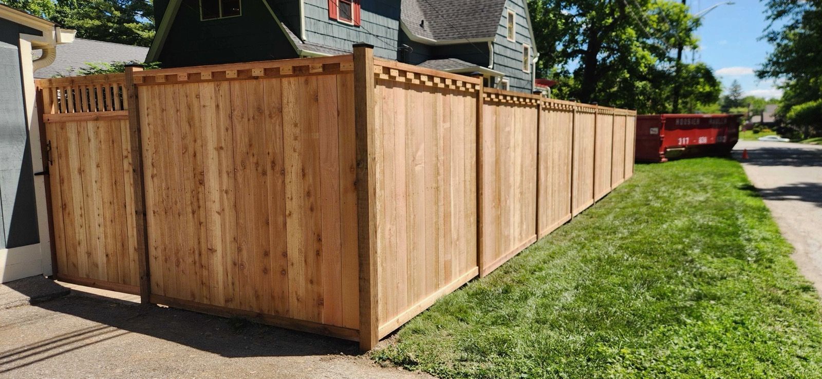 Wooden privacy fence along a sidewalk beside a grassy street on a sunny day