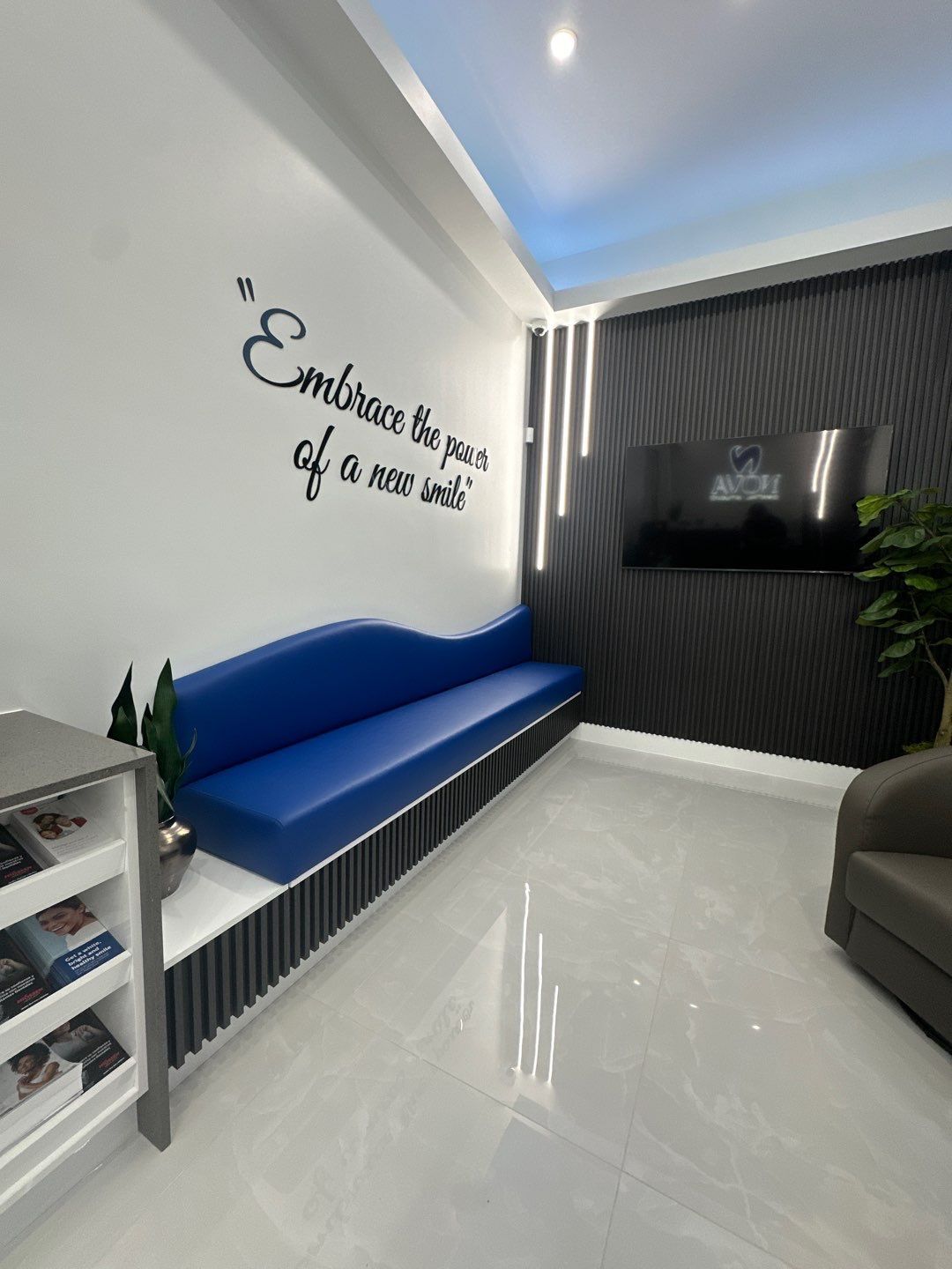 A waiting room with a blue couch and a tv on the wall.
