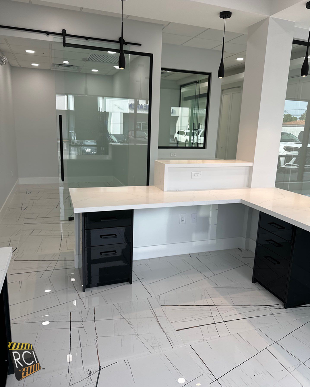 Empty modern office with a light wood desk, black cabinets, glass partitions, and tiled floor.