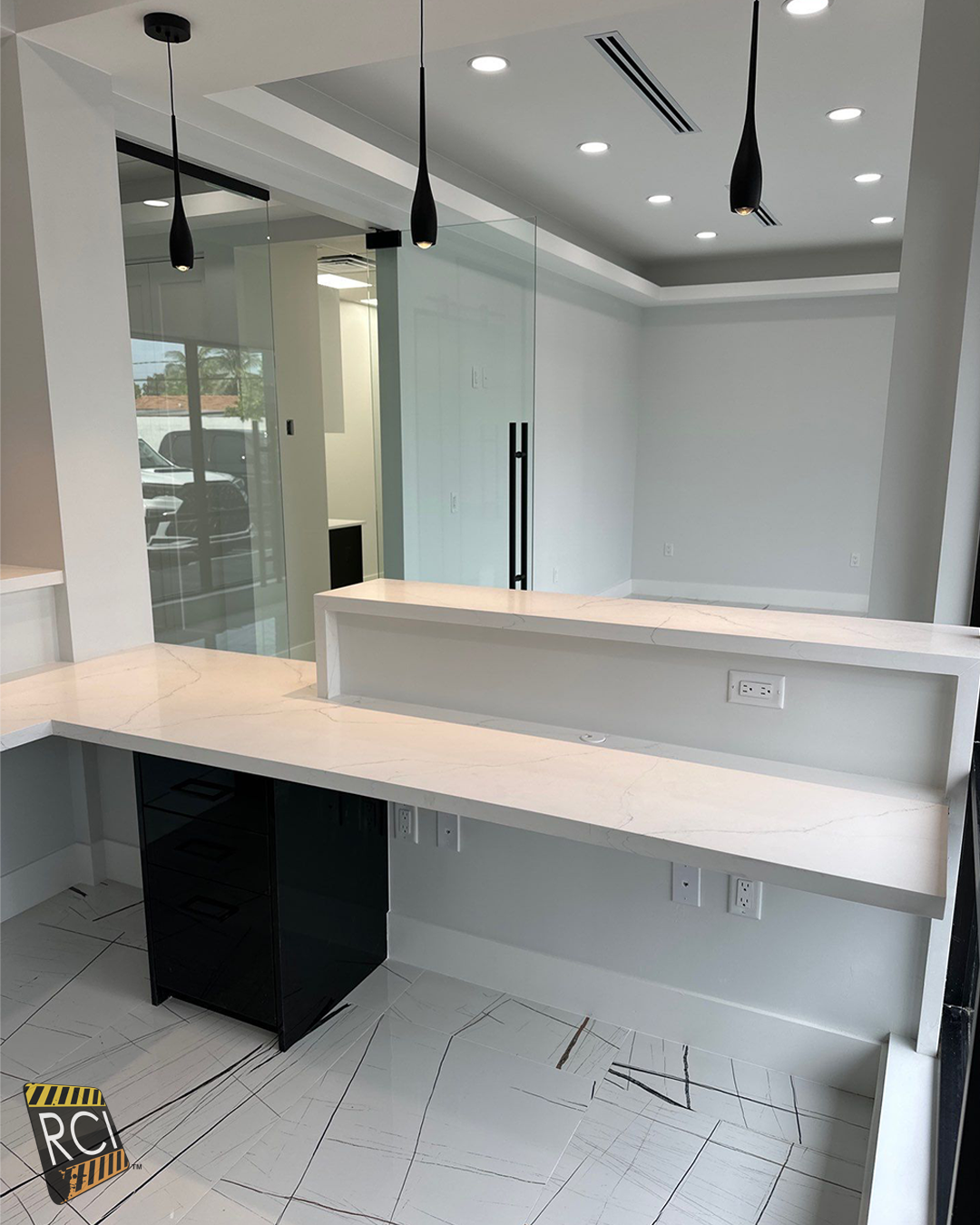 Modern white office reception area with glass walls, pendant lights, and a built-in desk