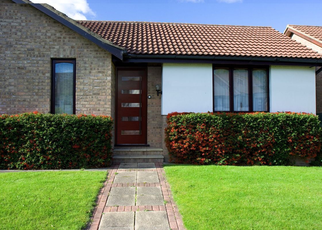 A house with a brick walkway leading to it and a lush green lawn.