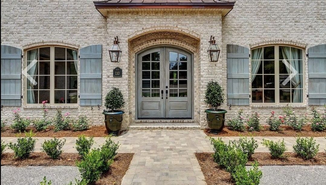 The front of a brick house with blue shutters and a walkway leading to the door.