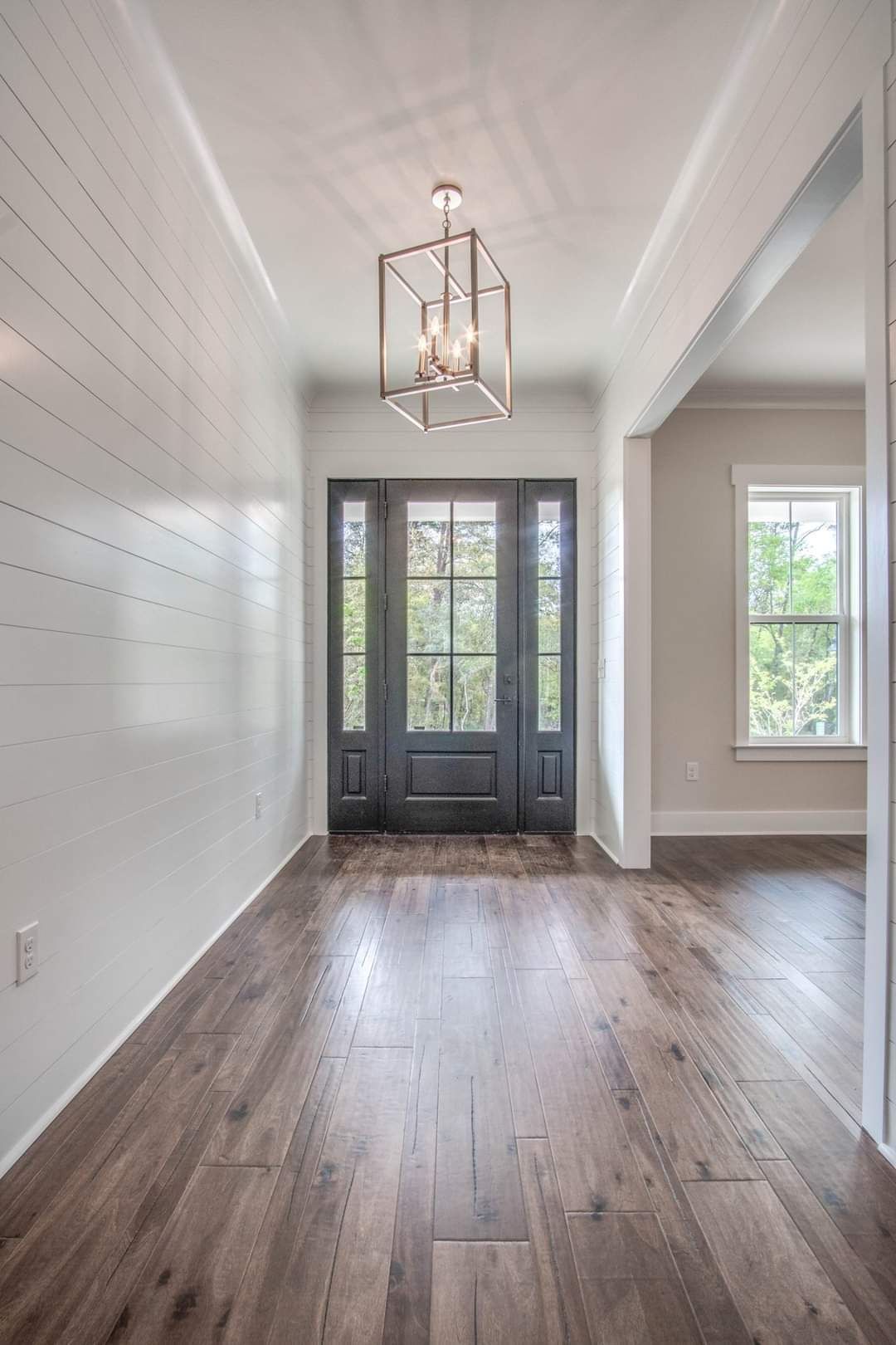 An empty hallway with hardwood floors and a chandelier hanging from the ceiling.
