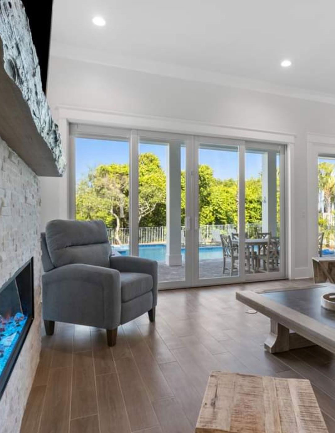 A living room with a fireplace , chair , coffee table and sliding glass doors.