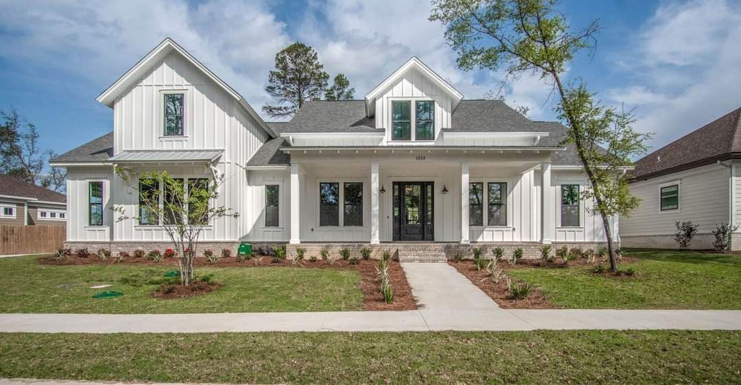 A large white house with a gray roof is sitting on top of a lush green lawn.