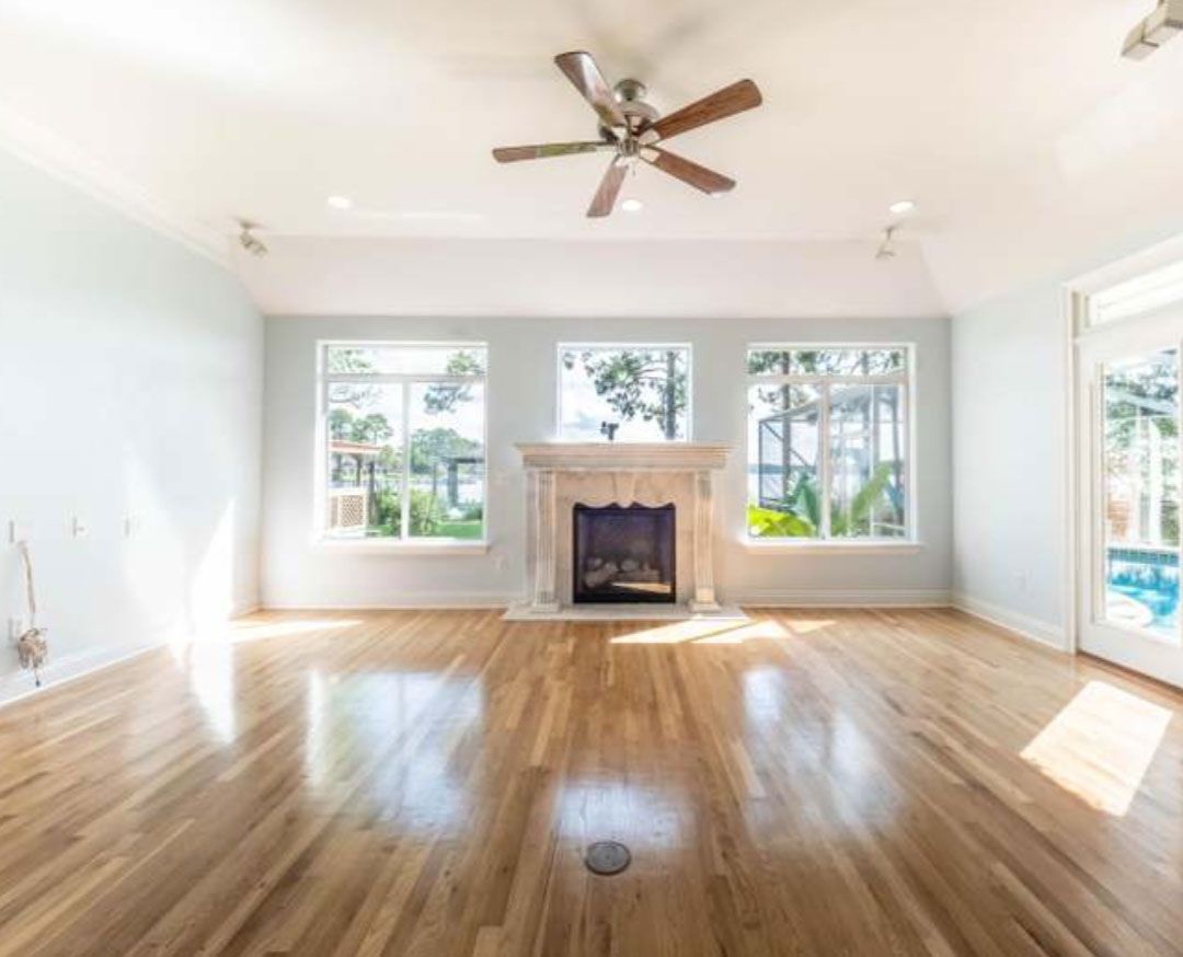 An empty living room with hardwood floors , a fireplace and a ceiling fan.