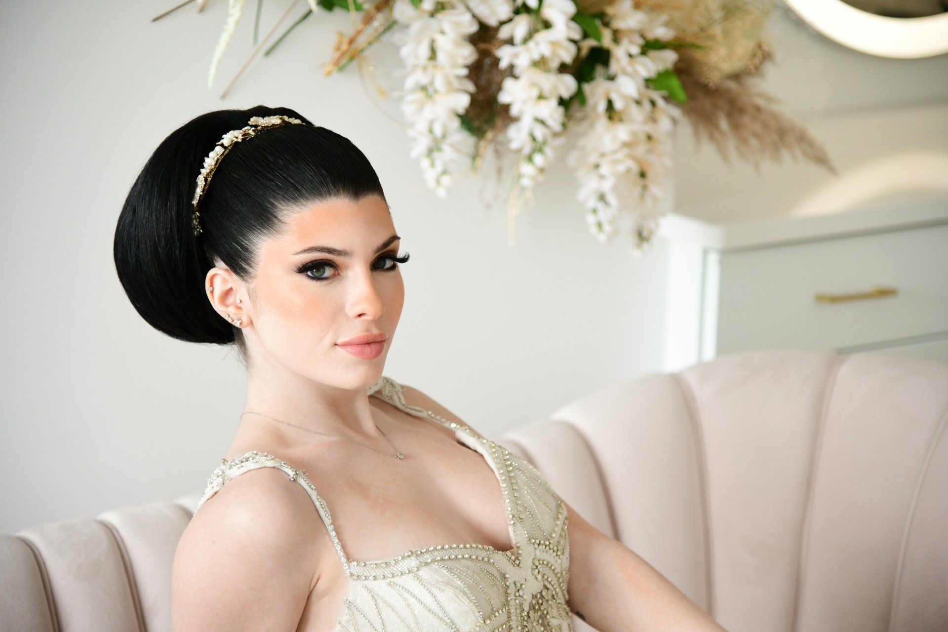 a woman in a wedding dress is sitting on a couch with flowers in the background