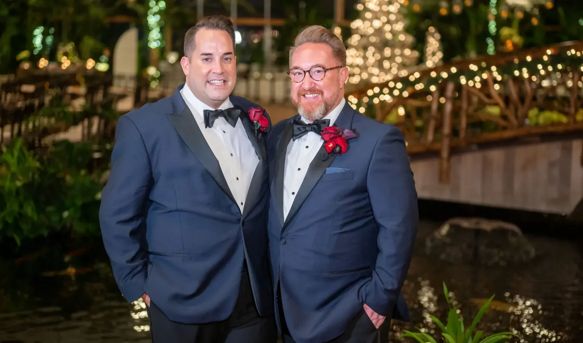 two men in tuxedos are posing for a picture in front of a bridge 
