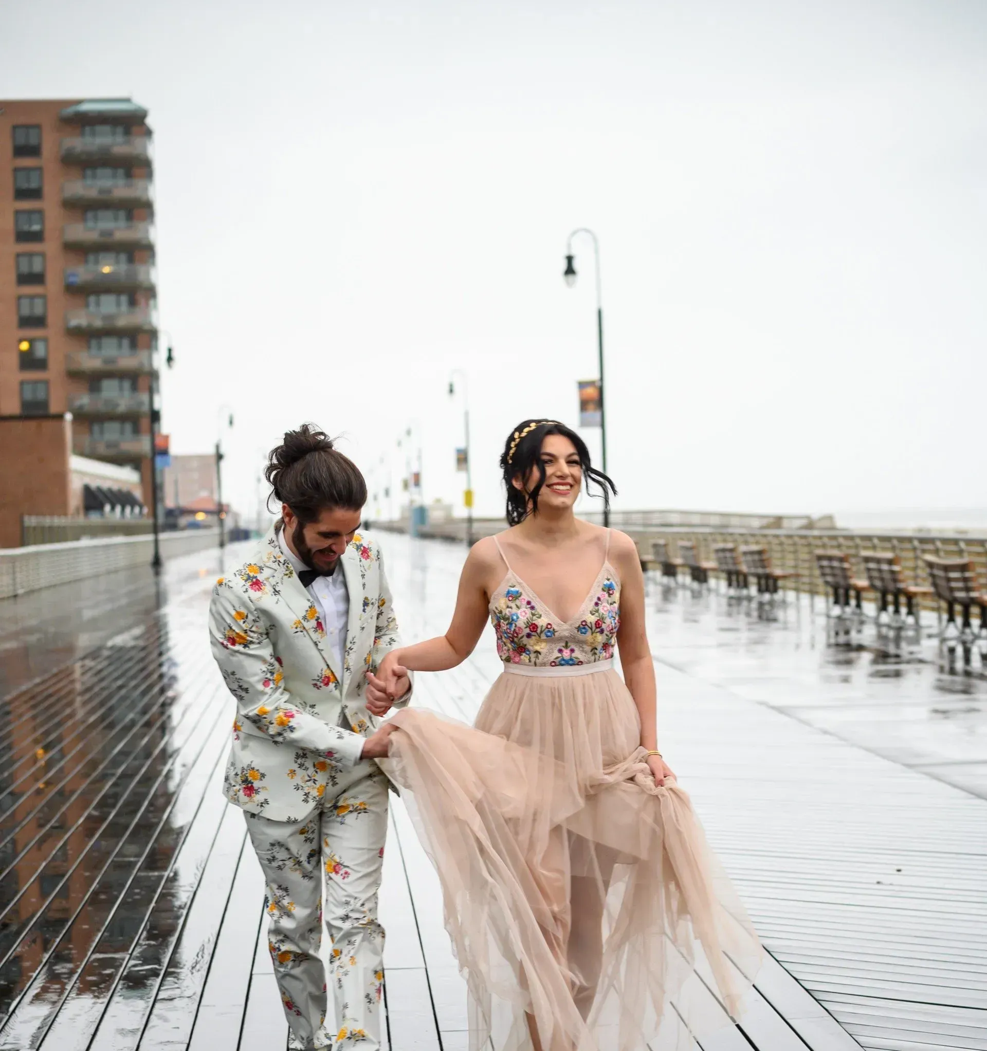 a man in a suit and a woman in a dress are walking on a boardwalk 