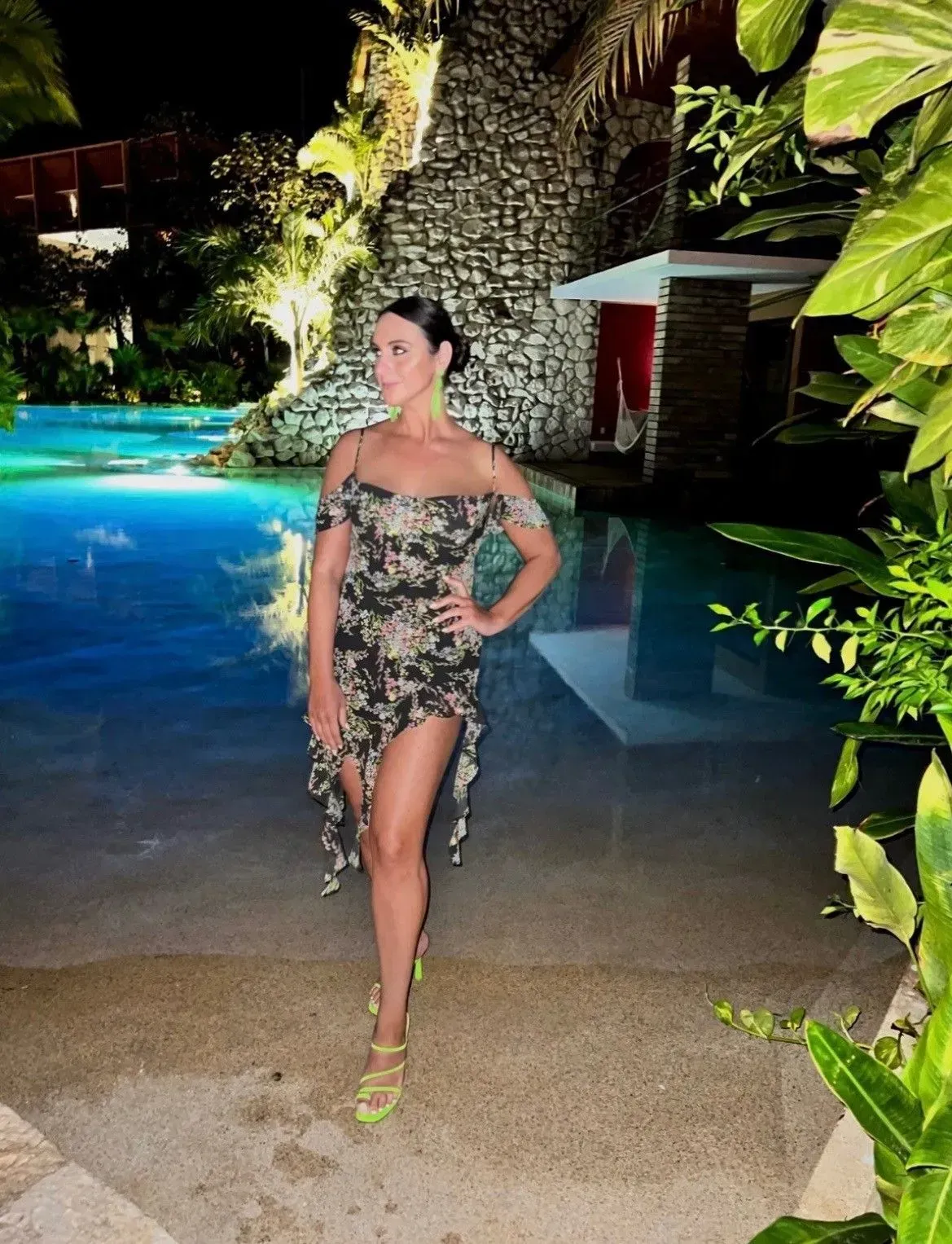 a woman in a dress is standing next to a pool at night