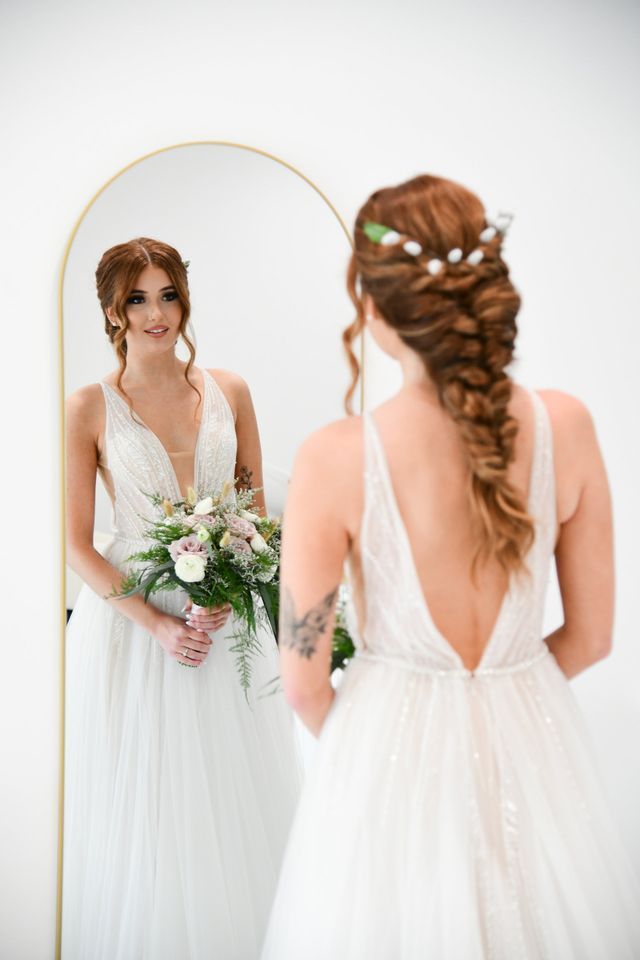 a woman in a wedding dress is standing in front of a mirror holding a bouquet of flowers