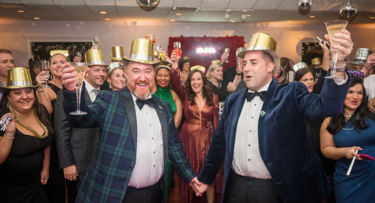 a group of people are standing in a room holding champagne glasses and wearing new year 's eve hats