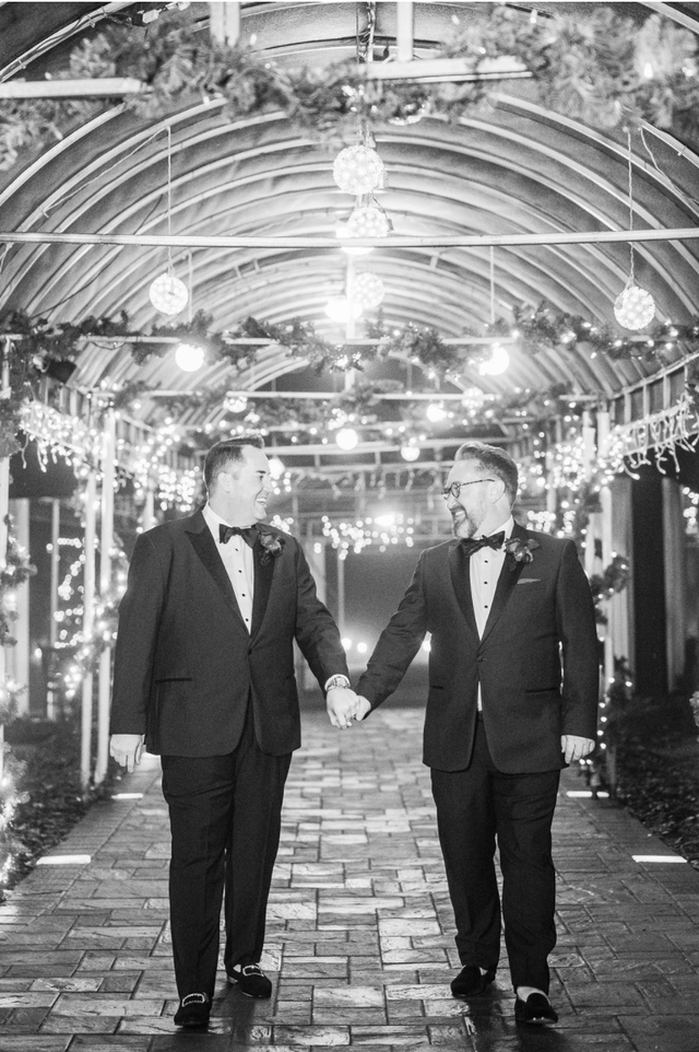 two men in tuxedos are holding hands in a black and white photo