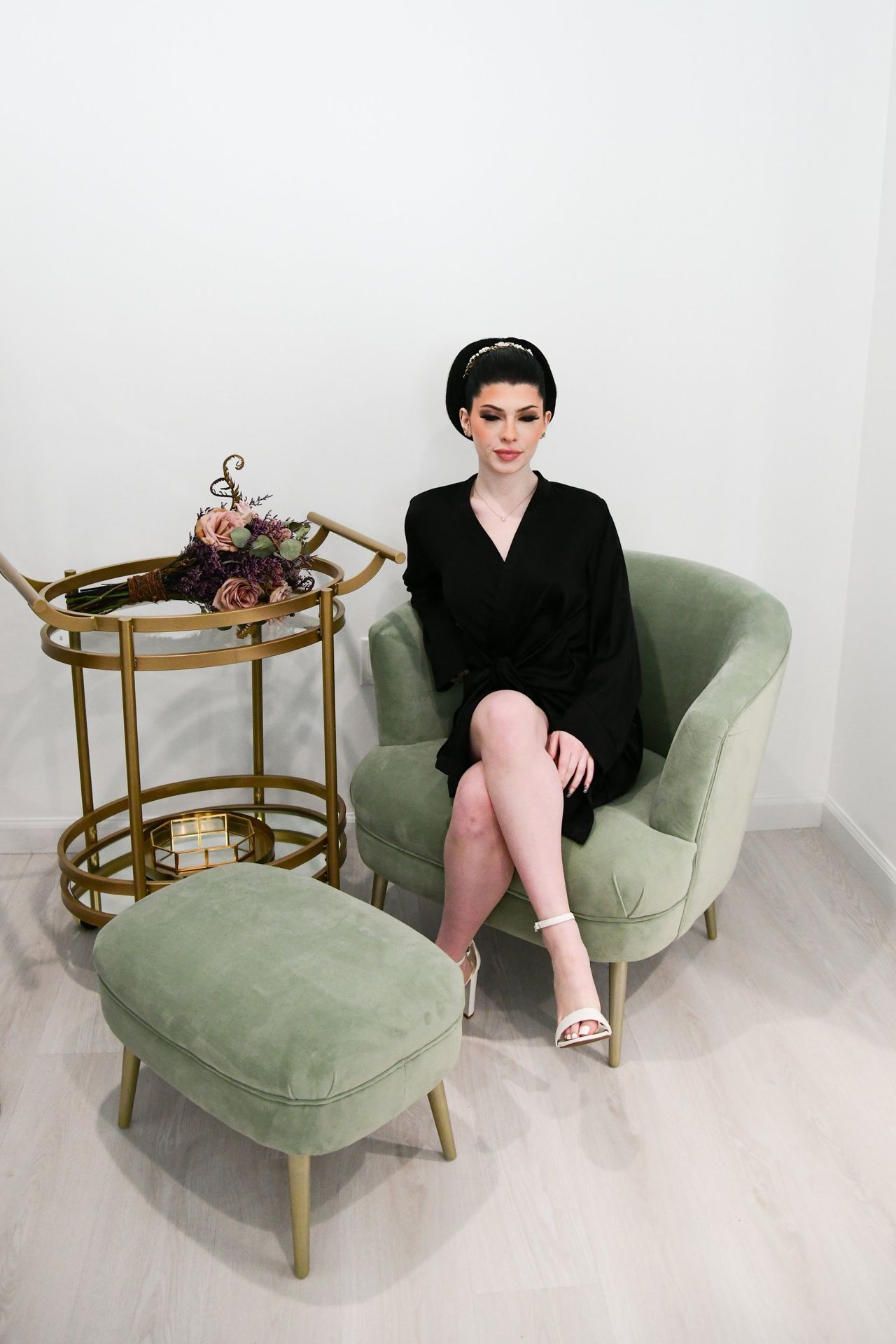 a woman in a black dress is sitting in a chair next to an ottoman