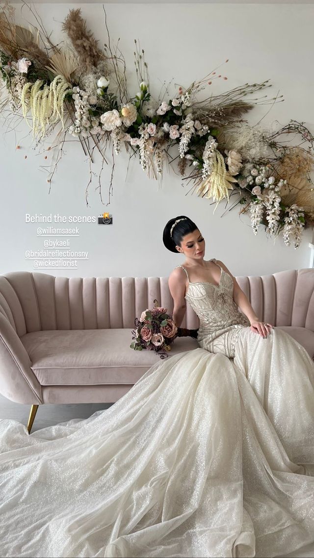 a bride in a wedding dress is sitting on a pink couch holding a bouquet of flowers