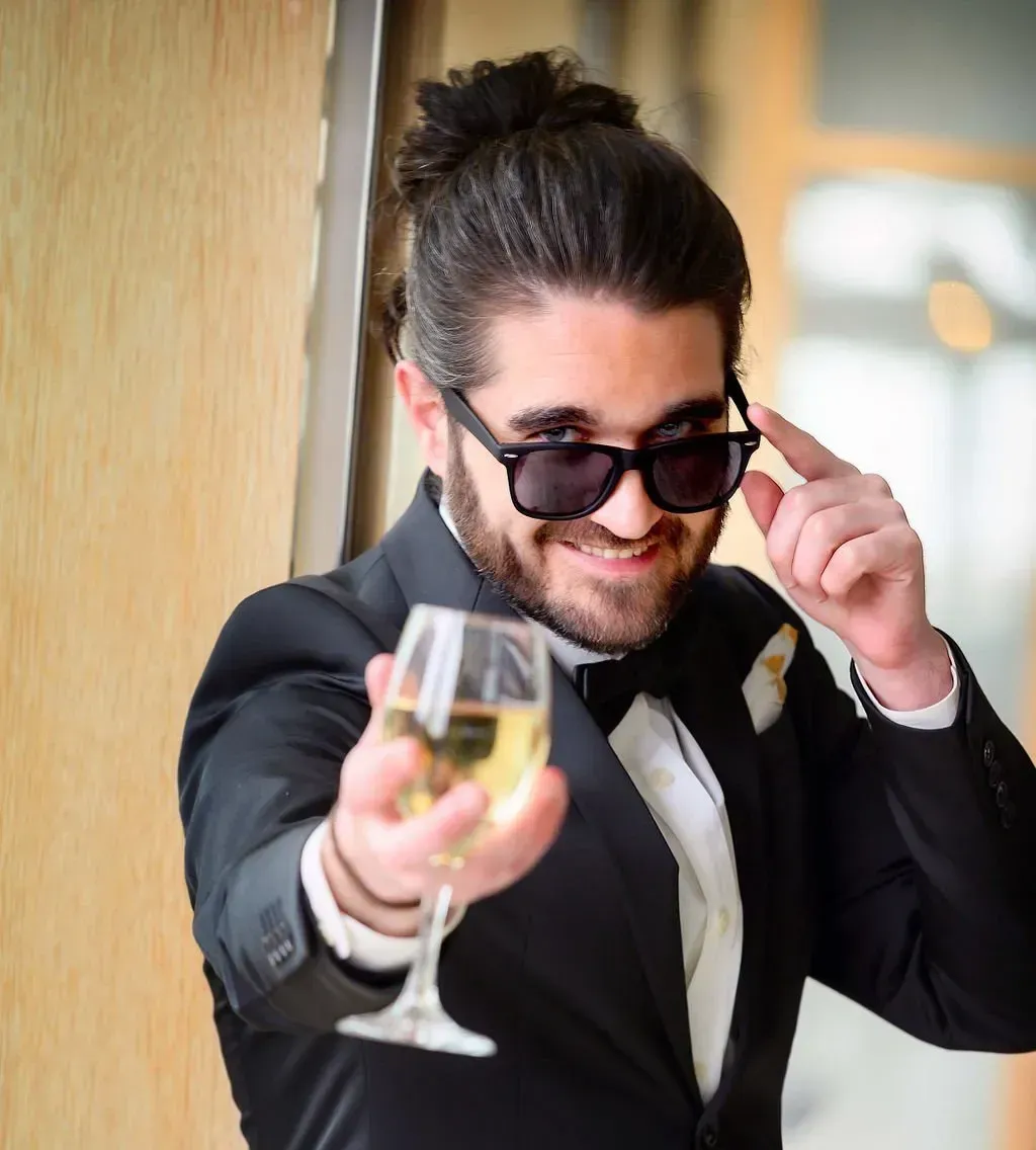 a man in a tuxedo and sunglasses is holding a glass of wine