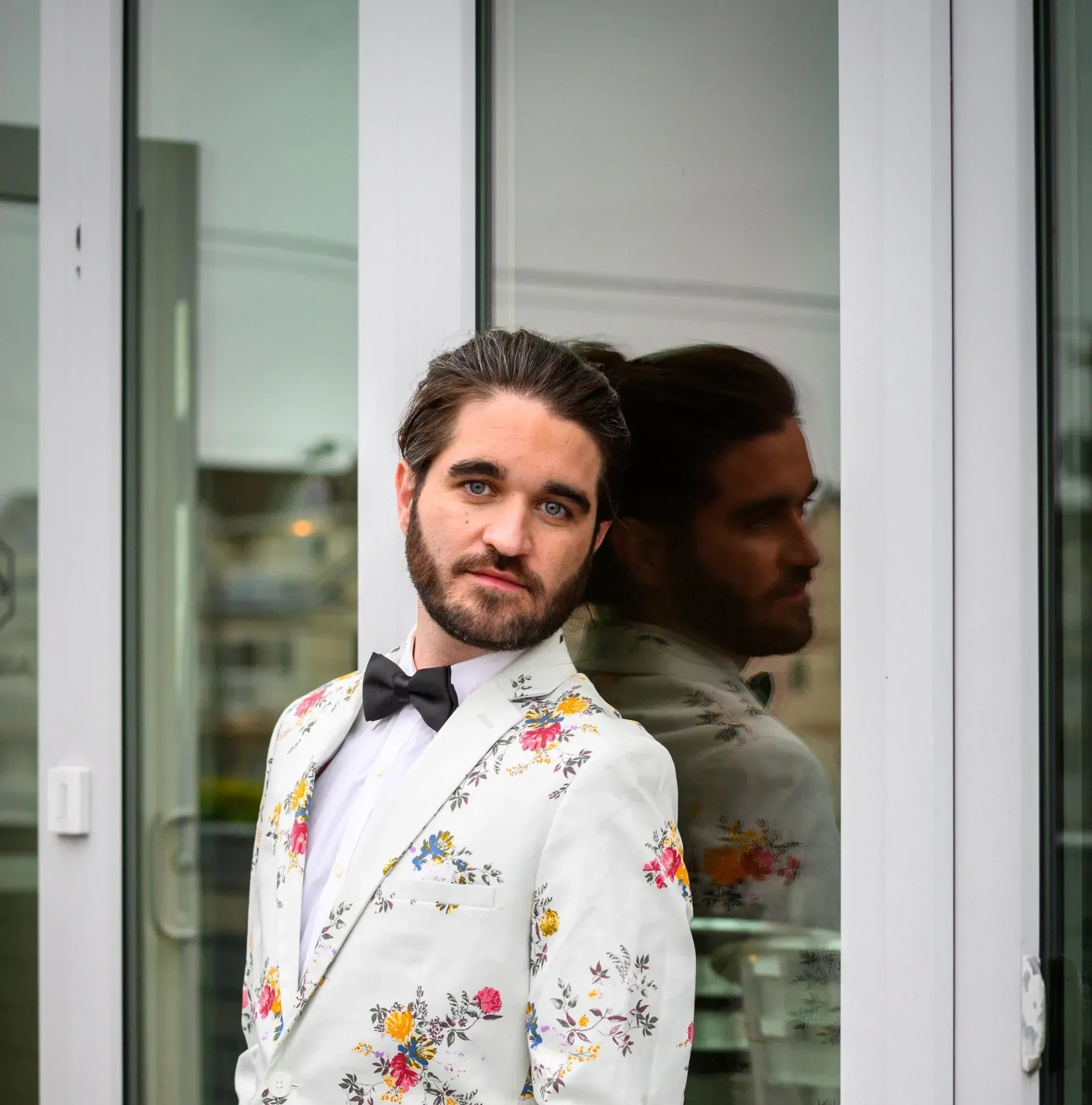 a man in a tuxedo and bow tie is standing in front of a glass door