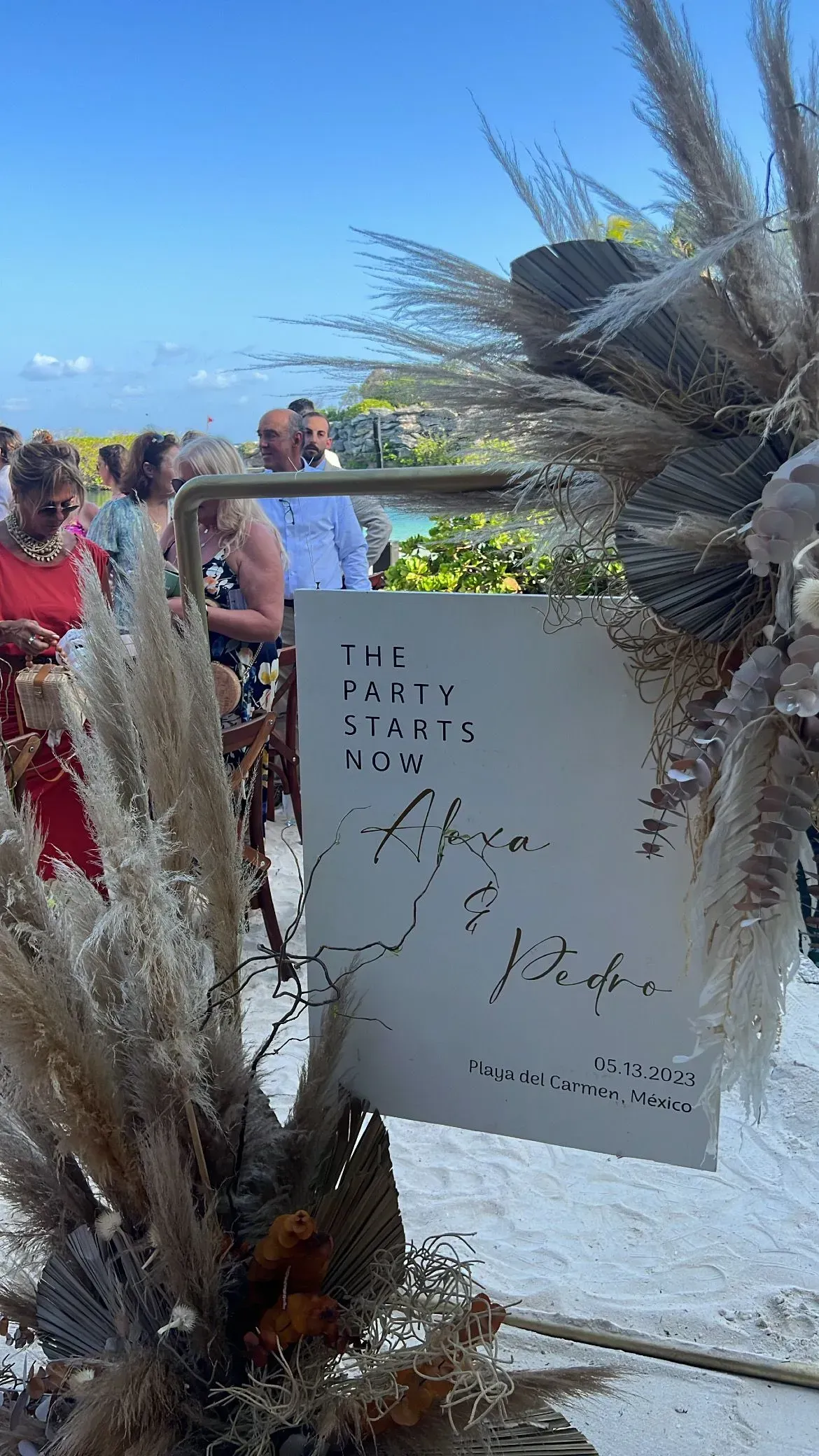 a white sign is sitting on top of a pile of dried flowers on a beach