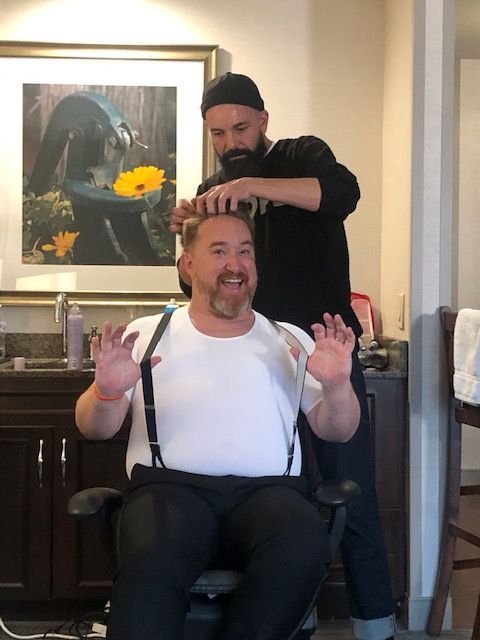 a man in suspenders is getting his hair cut by another man