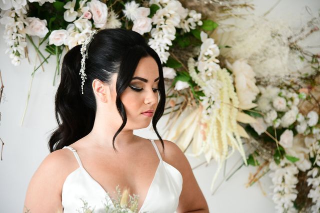 a woman in a white dress is standing in front of a wall of white flowers