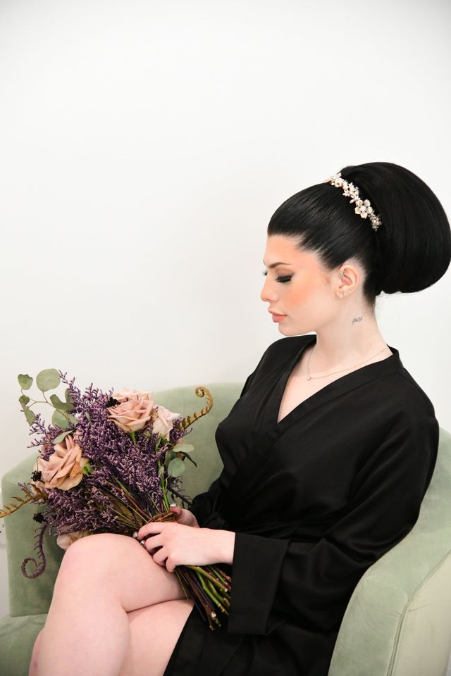 a woman in a black robe is sitting in a chair holding a bouquet of flowers