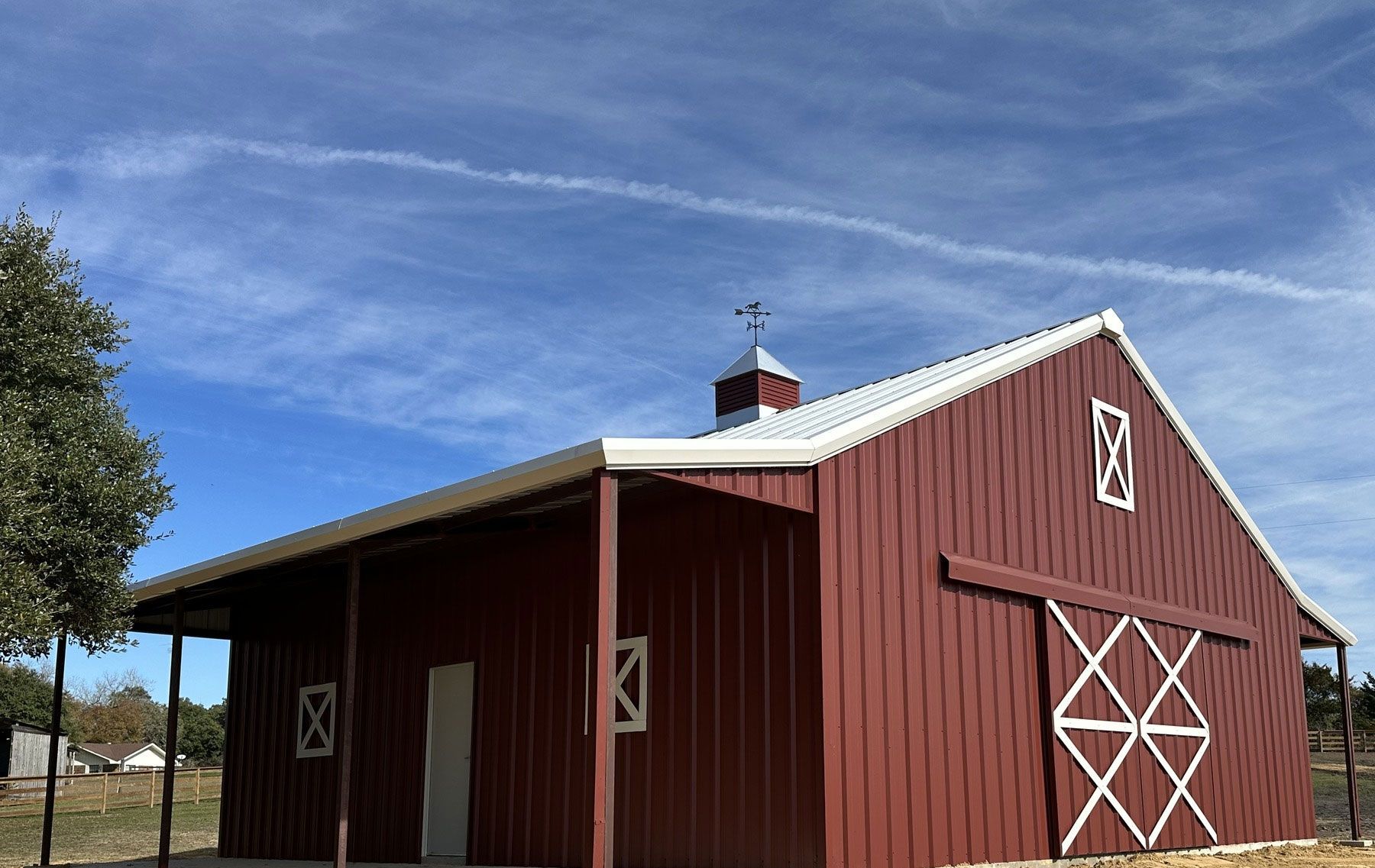 A red barn with a white roof and a porch on a sunny day.